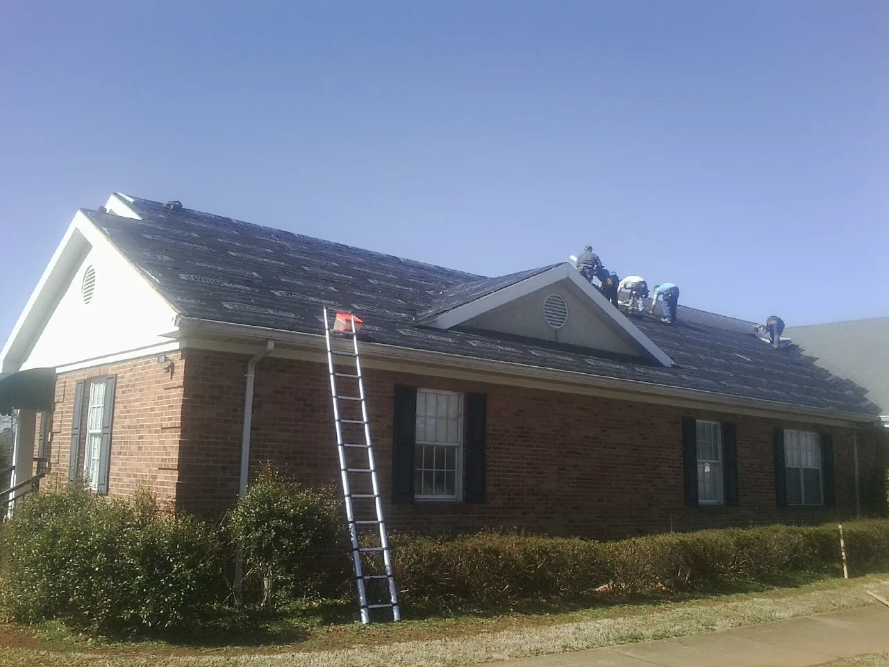 Crew tearing shingles off a brick ranch roof with a ladder set — Metal Roof Repair work by our crew in Sellersville