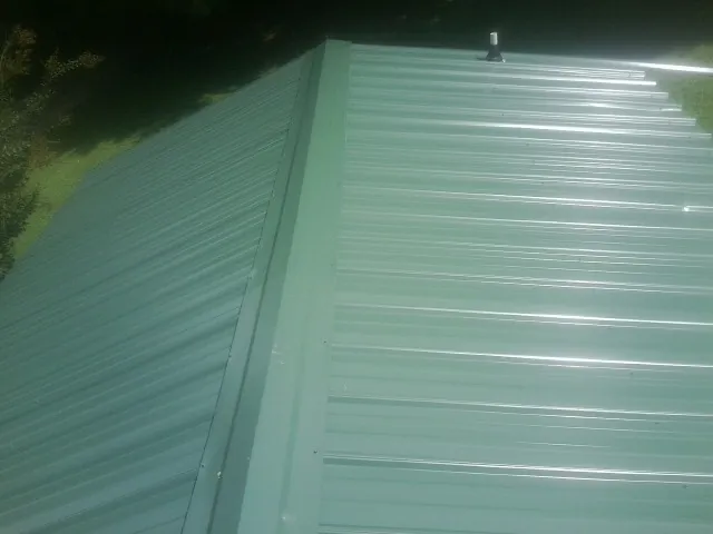 New green metal panels meeting at the ridge of a roof — Flat Roof Repair work by our crew in Sellersville