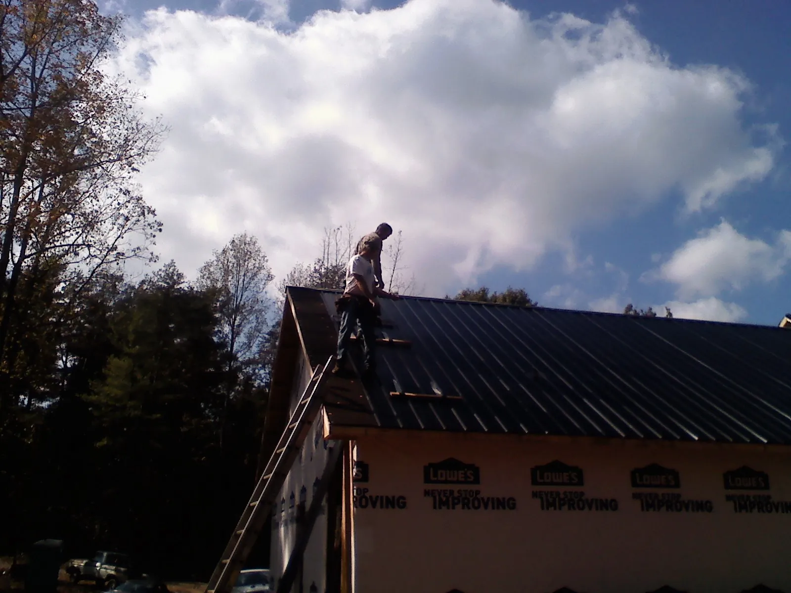 Roofer fastening dark metal panels high against a cloudy sky, from a Roof Inspection job in Sellersville