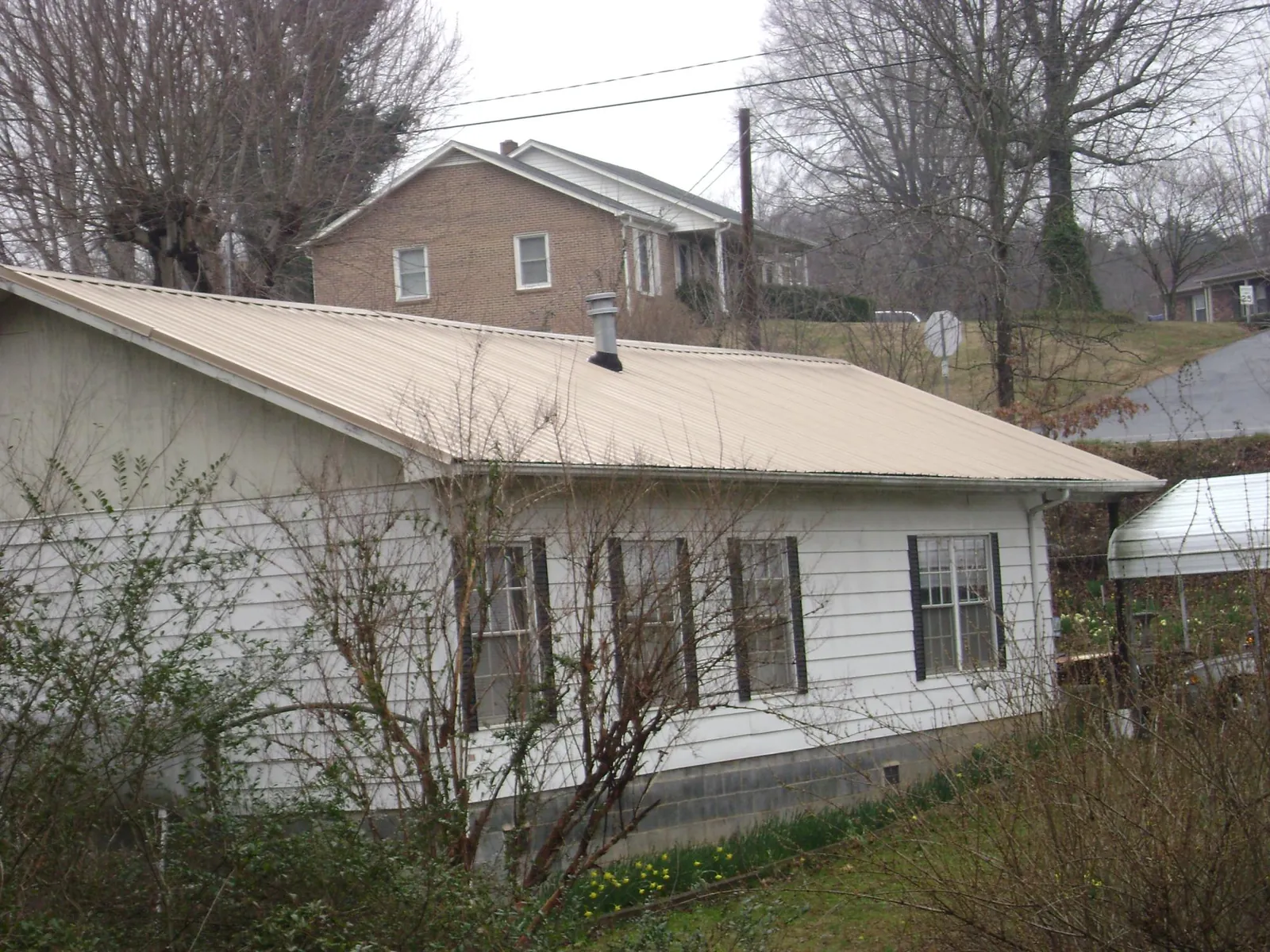 Tan metal roof on a white sided house set into a hillside — Commercial Roofing by Roofing Brothers in Sellersville